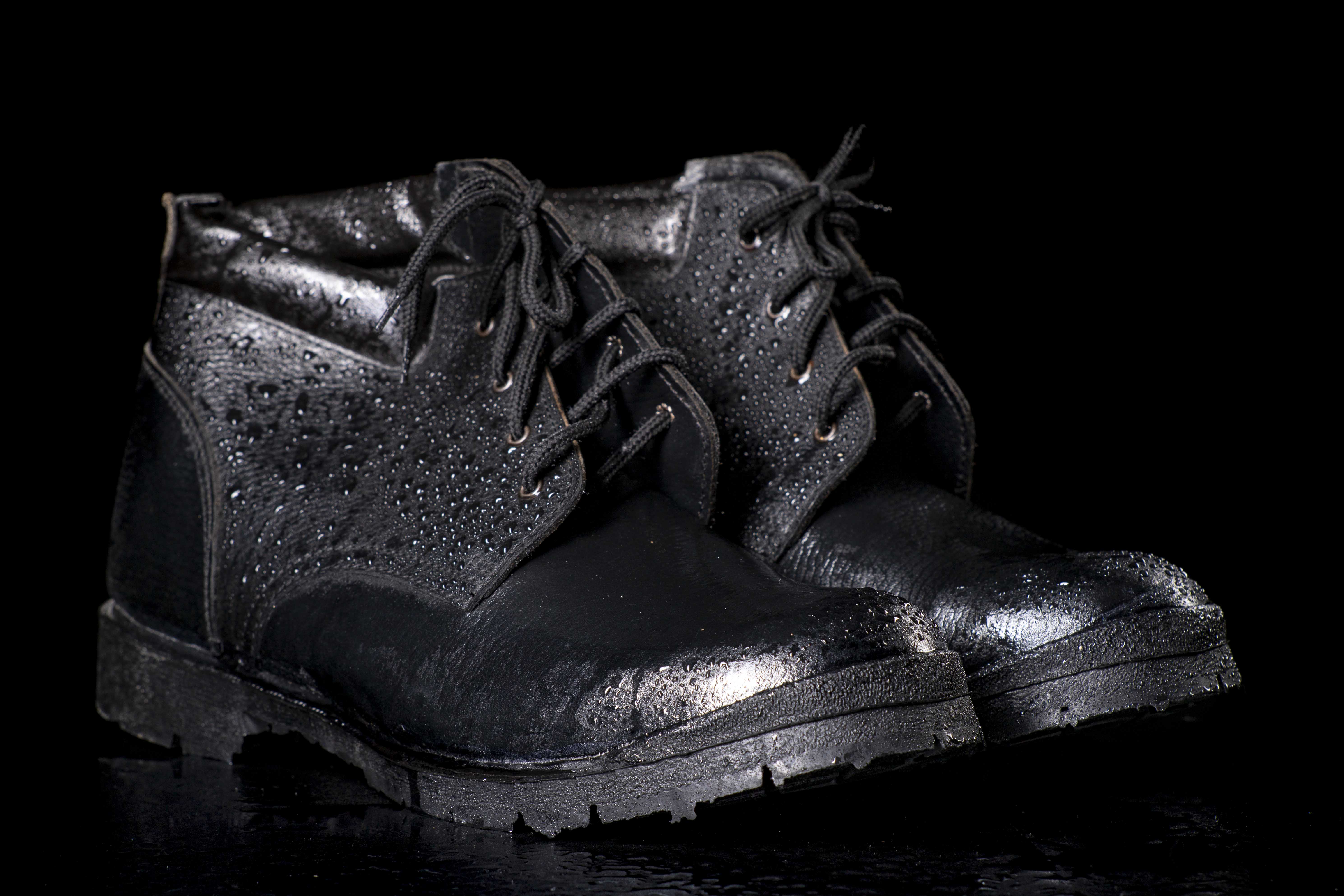 Black wet work boots on a dark table. Protective accessories for construction workers. Dark background.