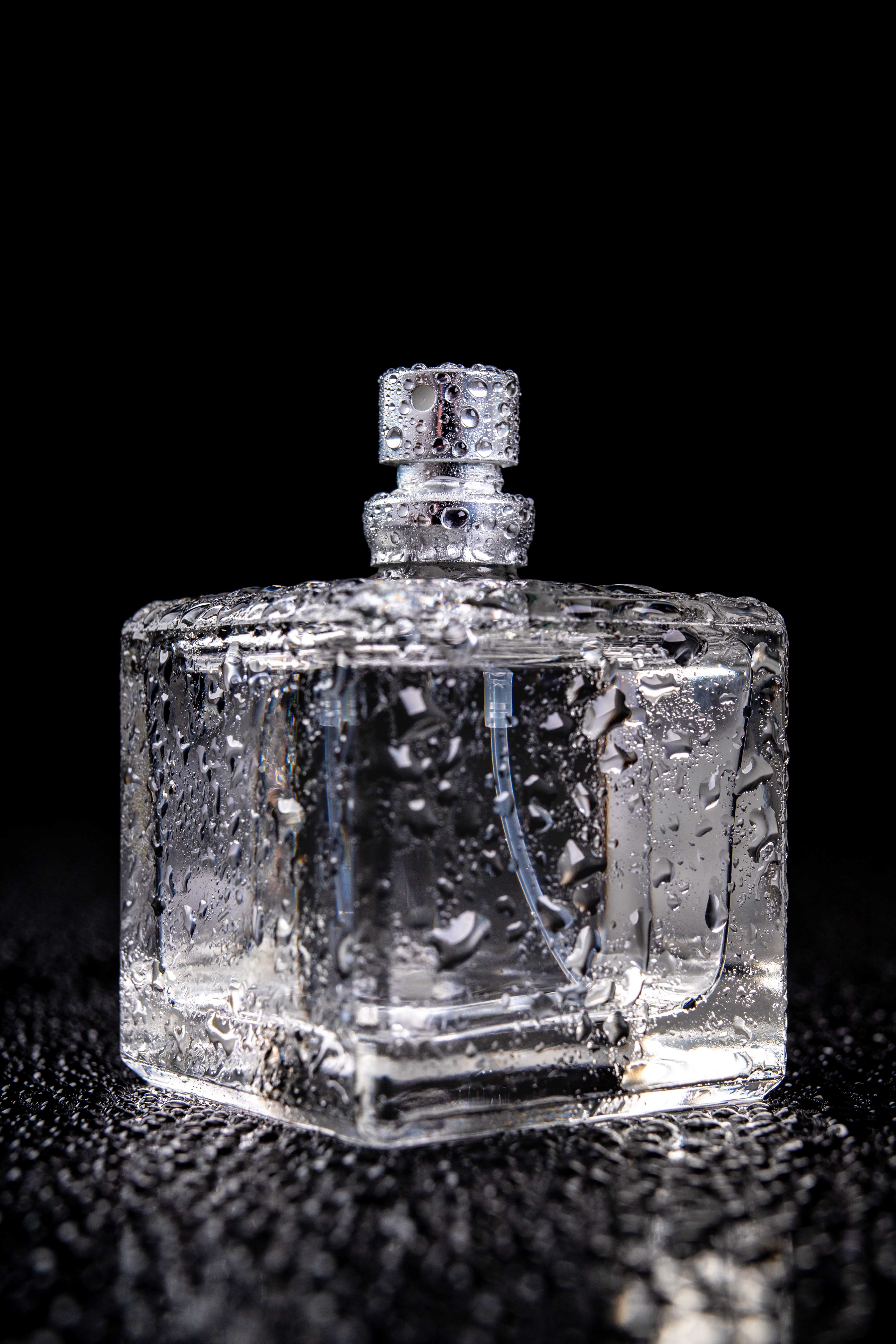Glass container with perfume covered with drops of water. A wet bottle with an atomizer. Dark background.