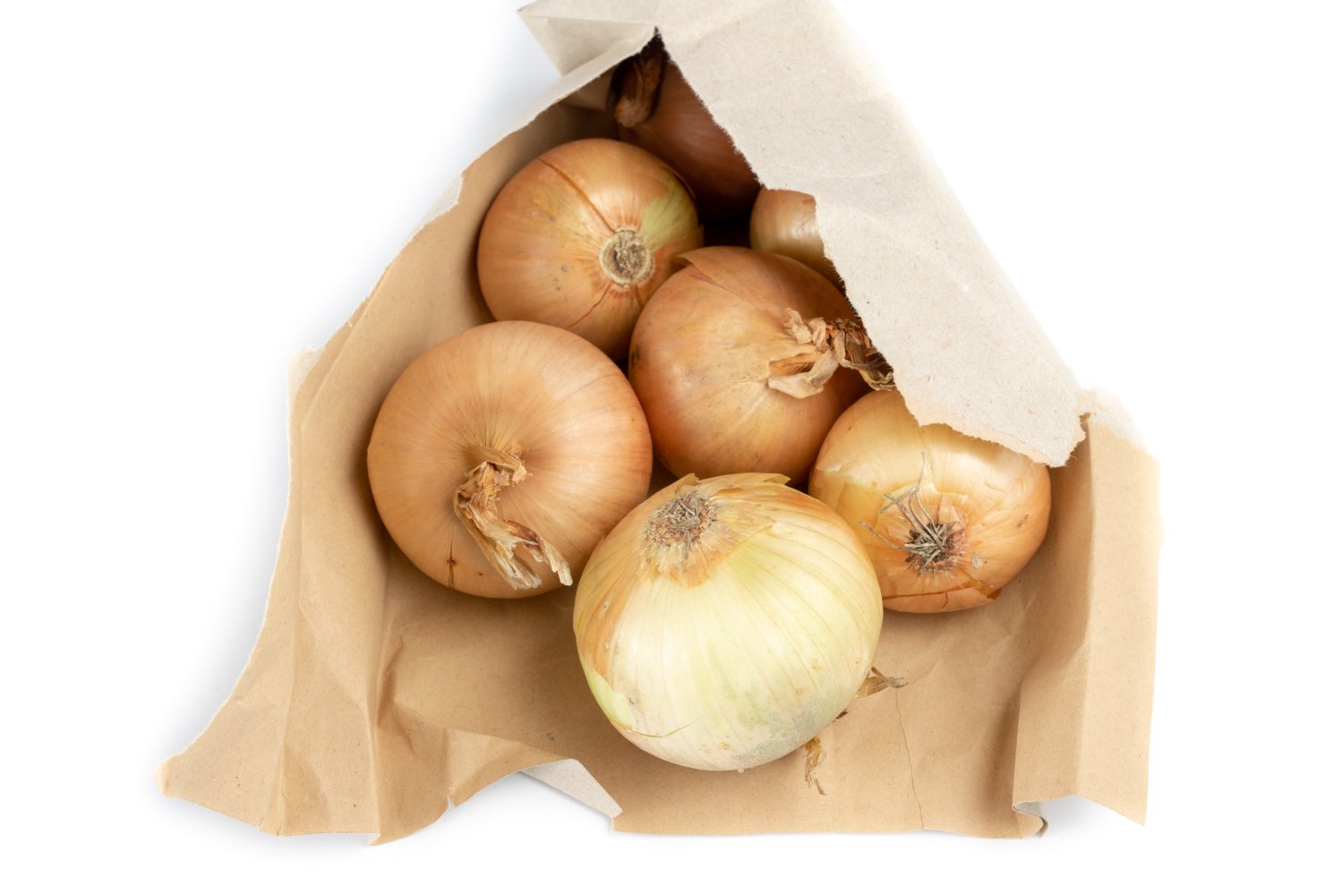 Onion in a paper bag on a white kitchen table. Vegetables for preparing dishes in the home kitchen. White background.