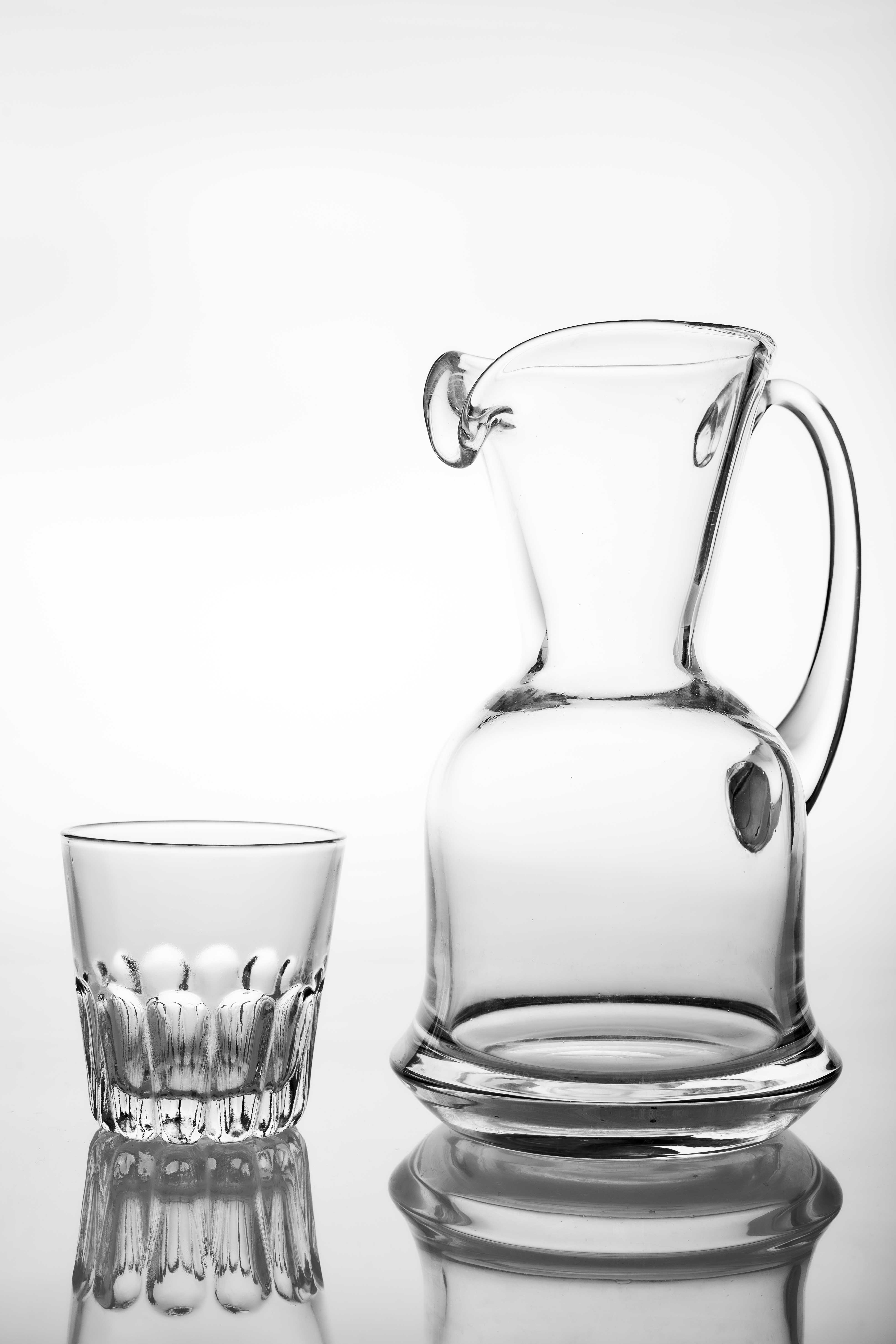Slim glass water jug and glass. Containers for feeding water in the household. Light background.