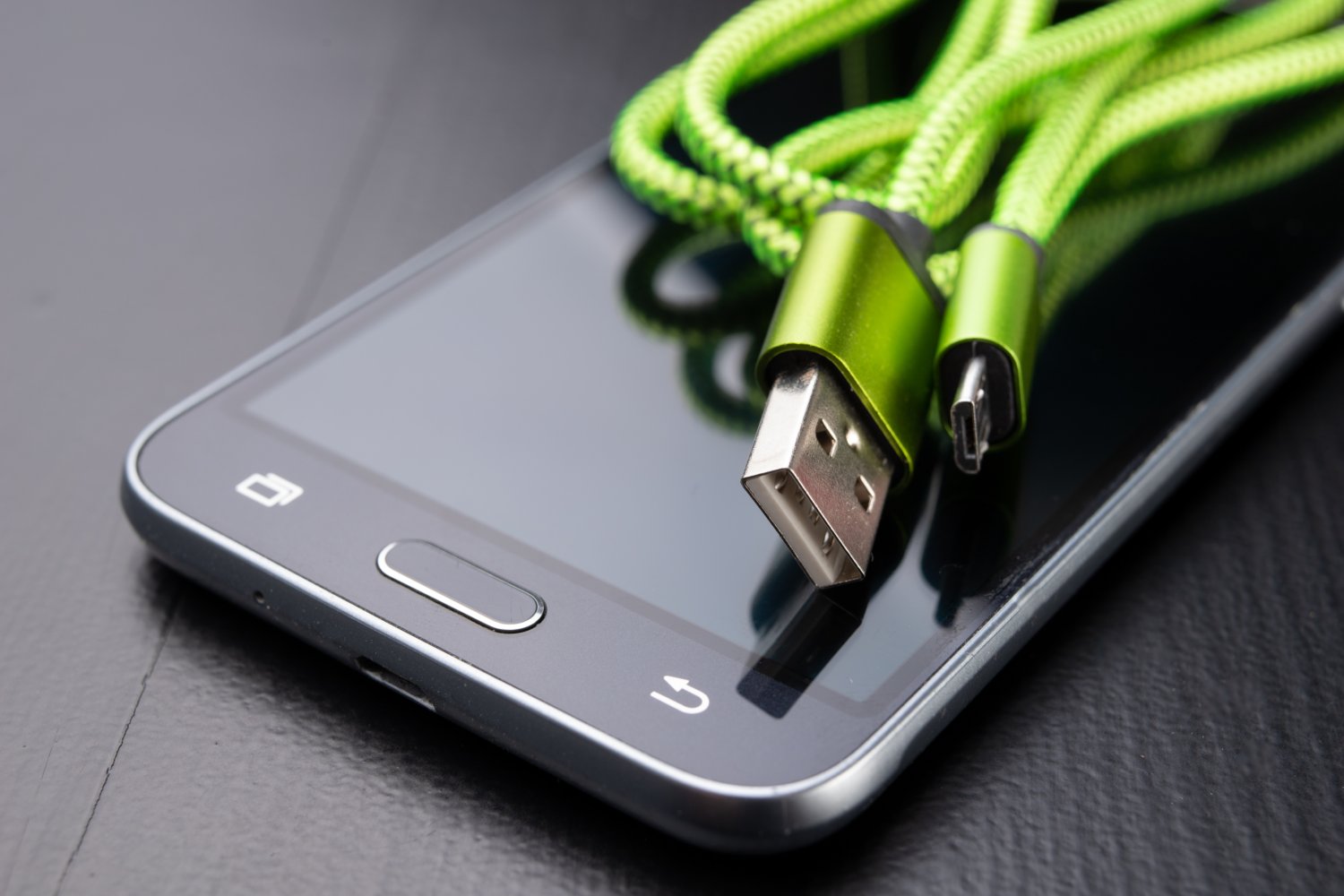 A usb cable for data transfer and phone charging. Telephone and accessories on the table. Dark background.