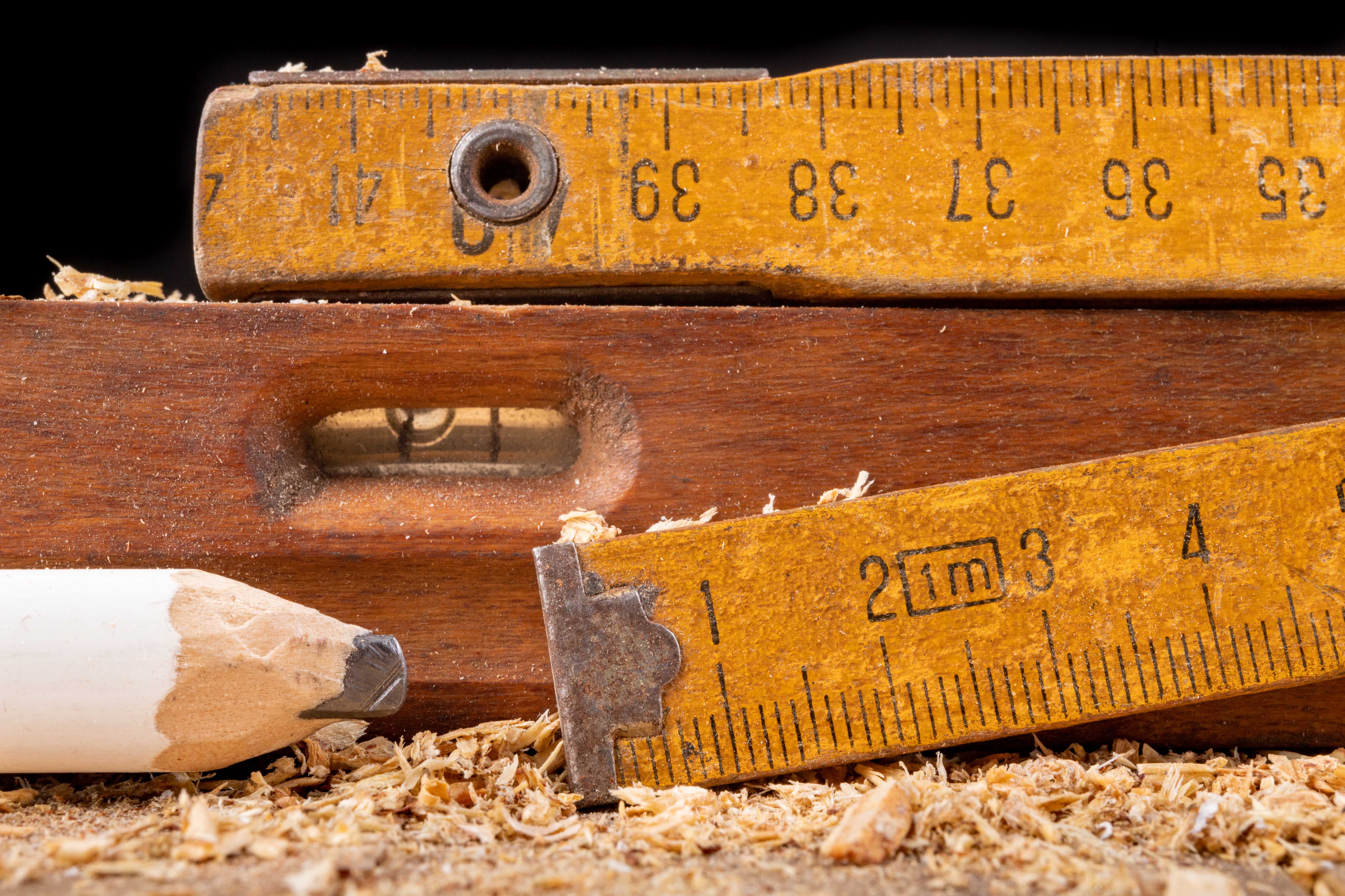 Carpentry measure, spirit level and pencil in sawdust on wooden table. Small carpentry work in a home workshop. Dark background.